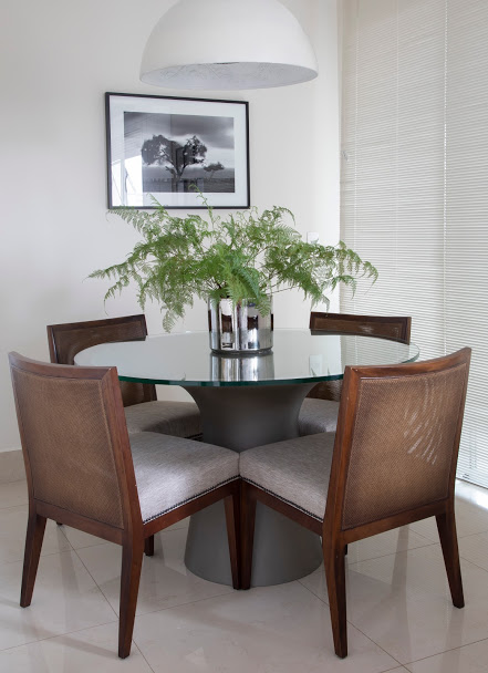 Sala de almoço branca, mesa de madeira e persiana plissada.